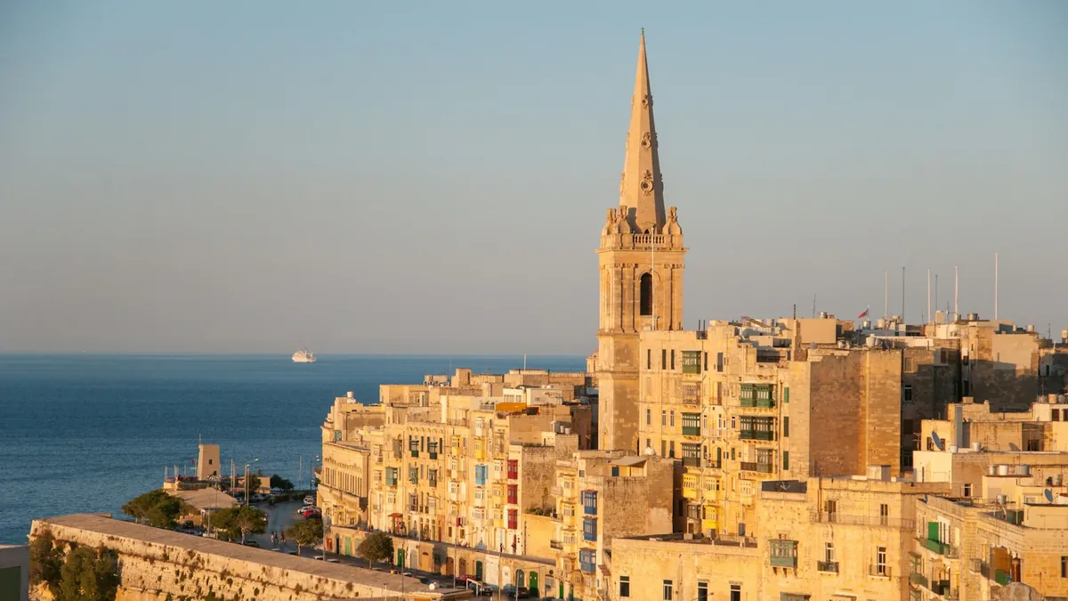 Valletta, Malta at golden hour, with limestone apartment buildings and a church spire above the Mediterranean